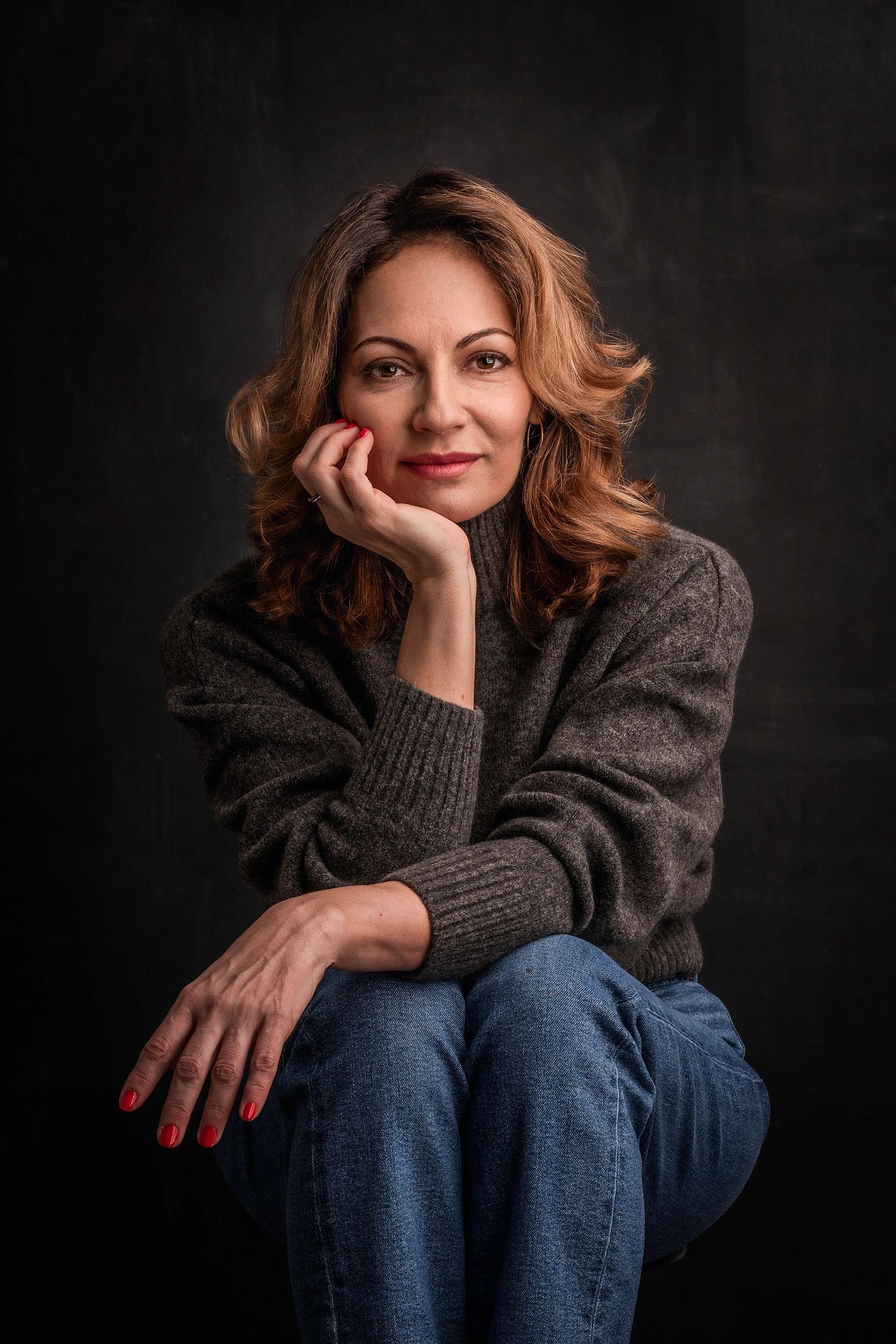 Mid aged woman seated against a dark background in a portrait session