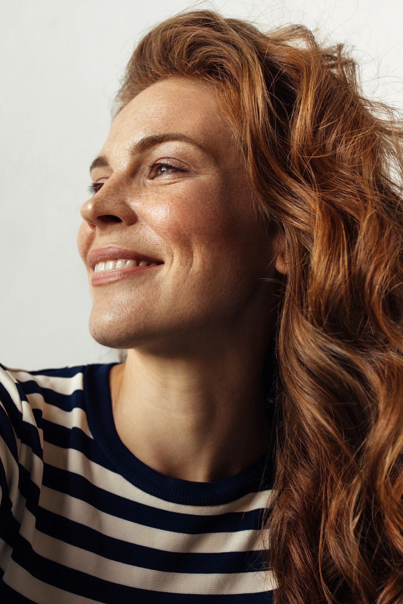 Smiling woman with flowing red hair in striped shirt looking to the side